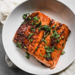 asian glazed spicy salmon in shallow white bowl with cilantro garnish
