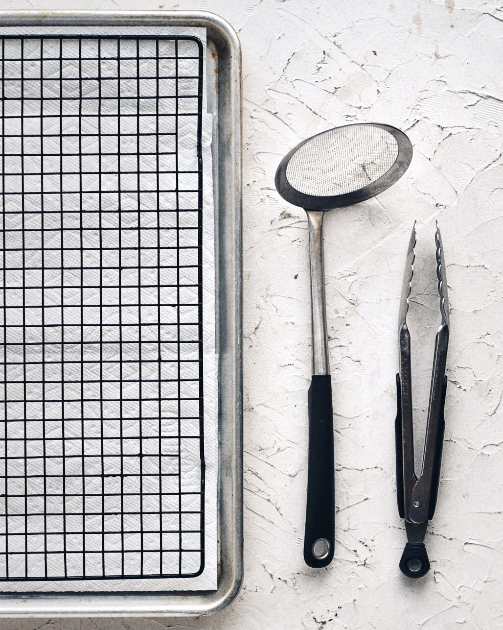 sheet pan lined with cooling rack next to spider strainer and tongs