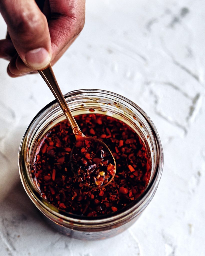 hand holding spoonful of chinese chili oil in glass jar