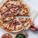 hand taking a slice of kimchi bacon pizza from a big wheel