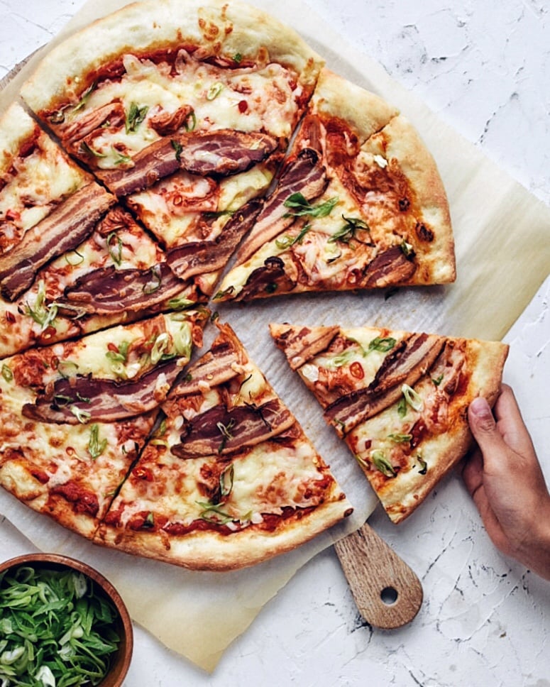 hand taking a slice of kimchi bacon pizza from a big wheel