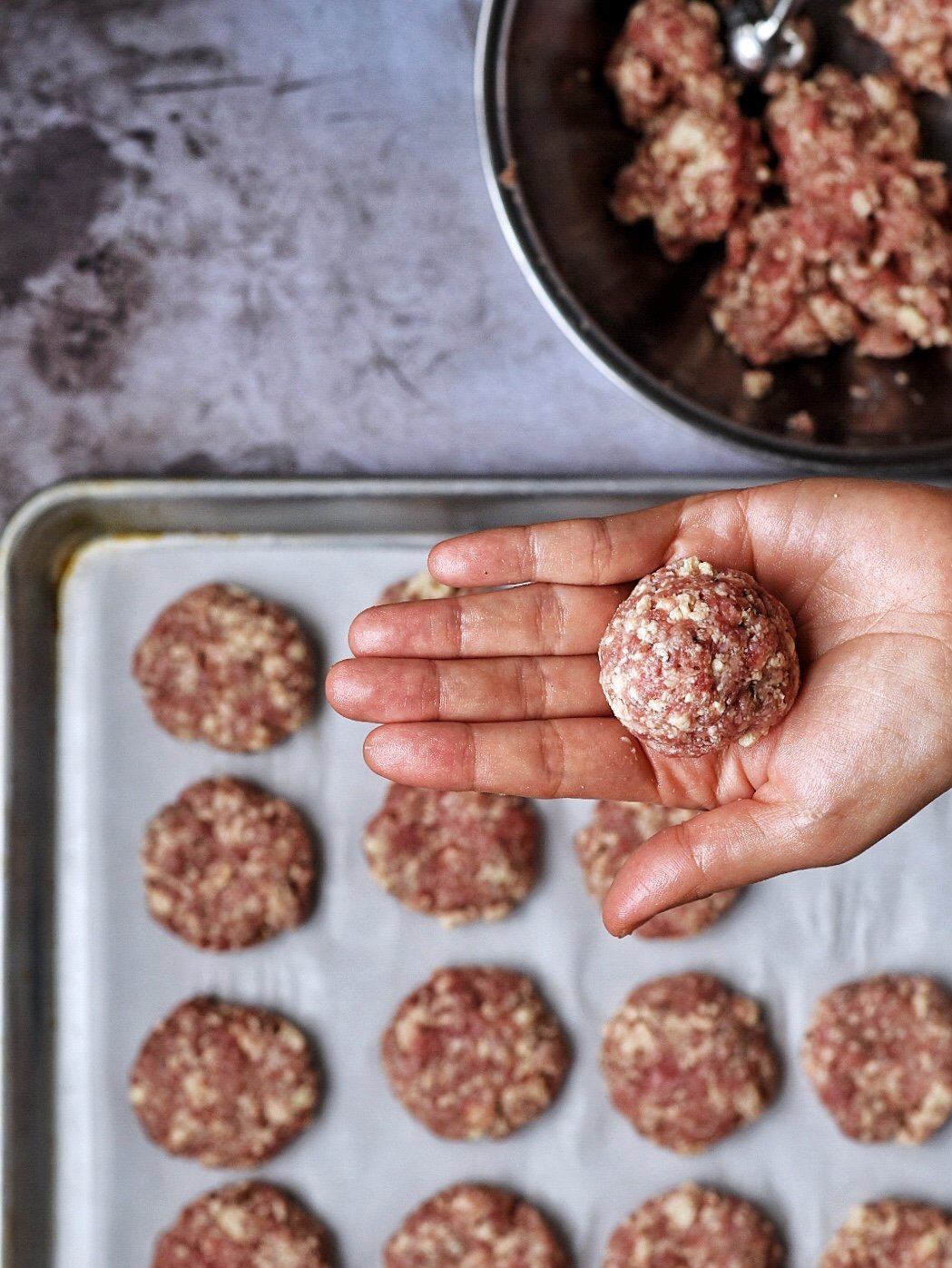 hand hold beef meatball with sheet pan underneath