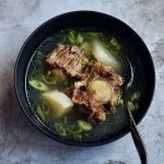 korean oxtail soup in black bowl with spoon on grey background