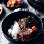 bowl of galbi jjim (Korean braised short ribs) with rice on grey napkin and wood table