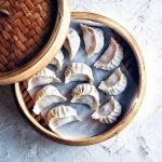bamboo steamer basket filled with fresh kimchi pork dumplings and lid partially off