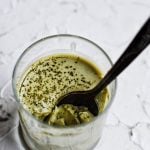 close up of glass cup filled with matcha coconut pudding with spoon digging in