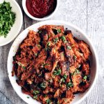 white bowl filled with gochujang pork on wood background with small bowl of gochujang on the side