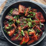 dubu jorim or korean braised tofu in dark shallow bowl with napkin and cutting board underneath