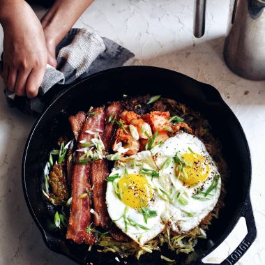 hands holding skillet full of egs, bacon, kimchi, hash browns