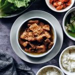 small shallow dish with korean braised pork belly and side dishes all around
