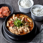bowl of korean soybean paste stew (doenjang jjigae) with two bowls of rice