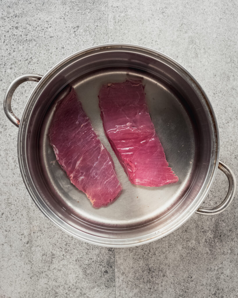 flank beef steak covered with water in pot