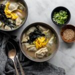 two bowls filled with korean rice cake soup with dumplings (tteok mandu guk)