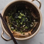 gold cooking pot filled with soba noodle soup with roasted nori and green onion garnish