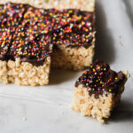 one rice krispie treat covered with a layer of chocolate with the rest of the pan nearby