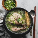 samgyetang (korean ginseng chicken soup) in black clay pot with spoon and chopsticks on the side