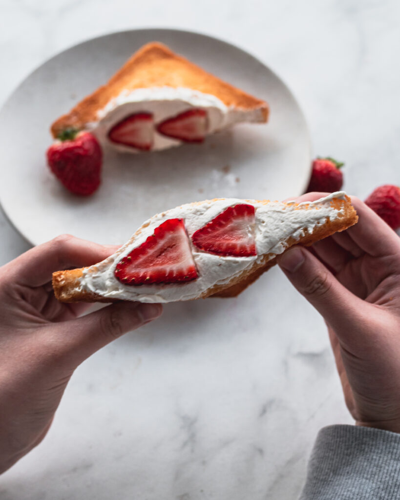 two hands holding a japanese fried cream sando with strawberries