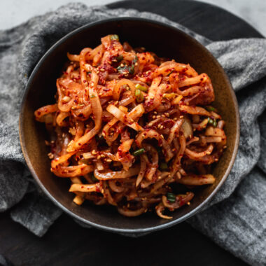 dark brown bowl filled with korean radish salad (musangchae) and grey napkin underneath