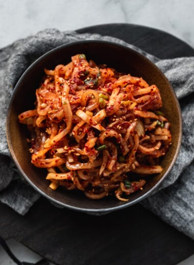 dark brown bowl filled with korean radish salad (musangchae) and grey napkin underneath