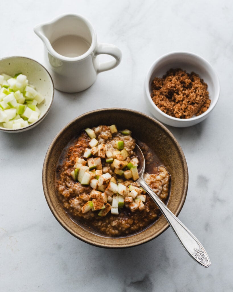 bowl of steel cut oats with cinnamon apple on breakfast table with spoon