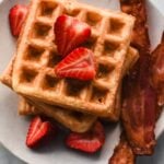 mochi waffles stacked on plate with strawberries and bacon