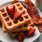 mochi waffles stacked on a plate with bacon and strawberries