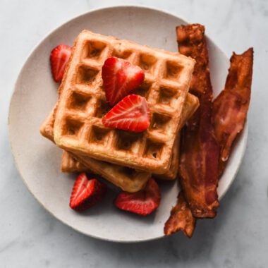 stacked mochi waffles on plate with bacon and strawberries