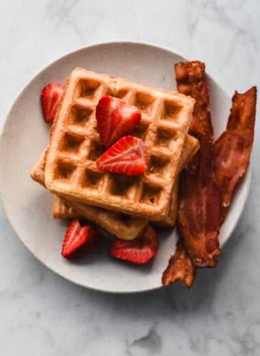 stacked mochi waffles on plate with bacon and strawberries