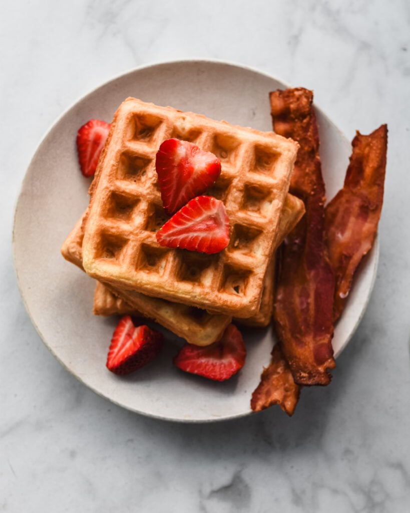 stacked mochi waffles on plate with bacon and strawberries