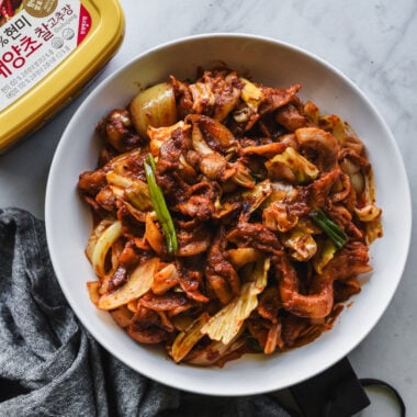 spicy korean pork on white serving platter with tub of gochujang nearby