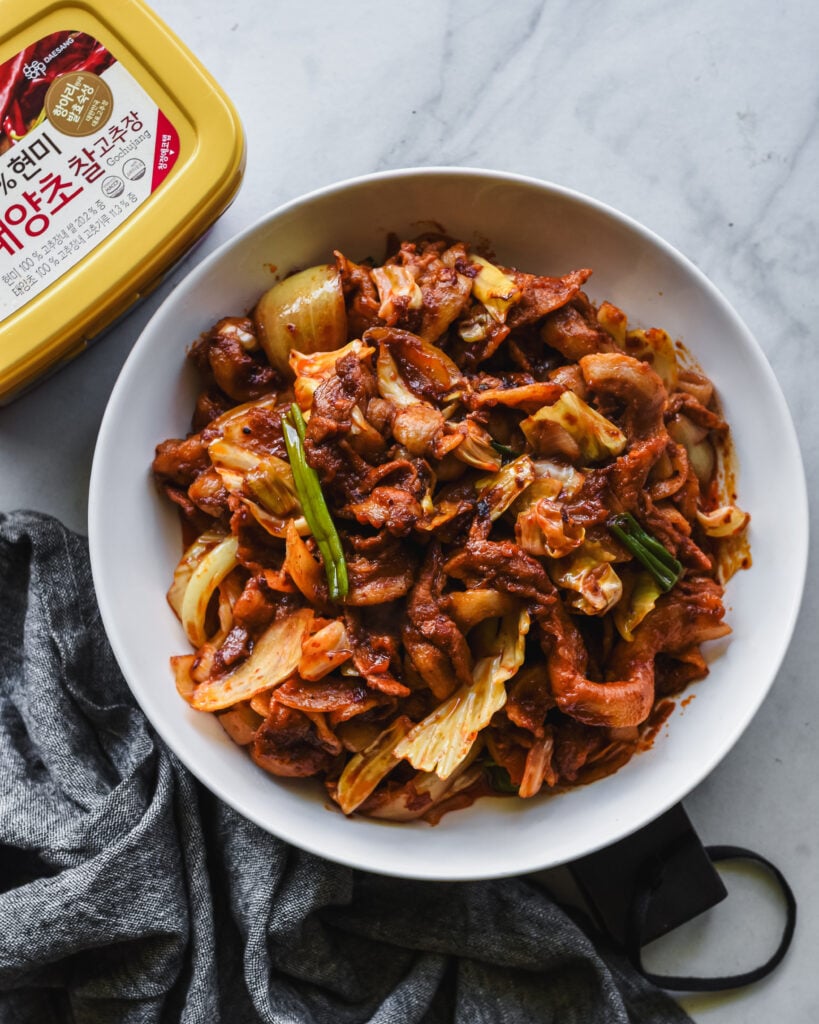 spicy korean pork on white serving platter with tub of gochujang nearby