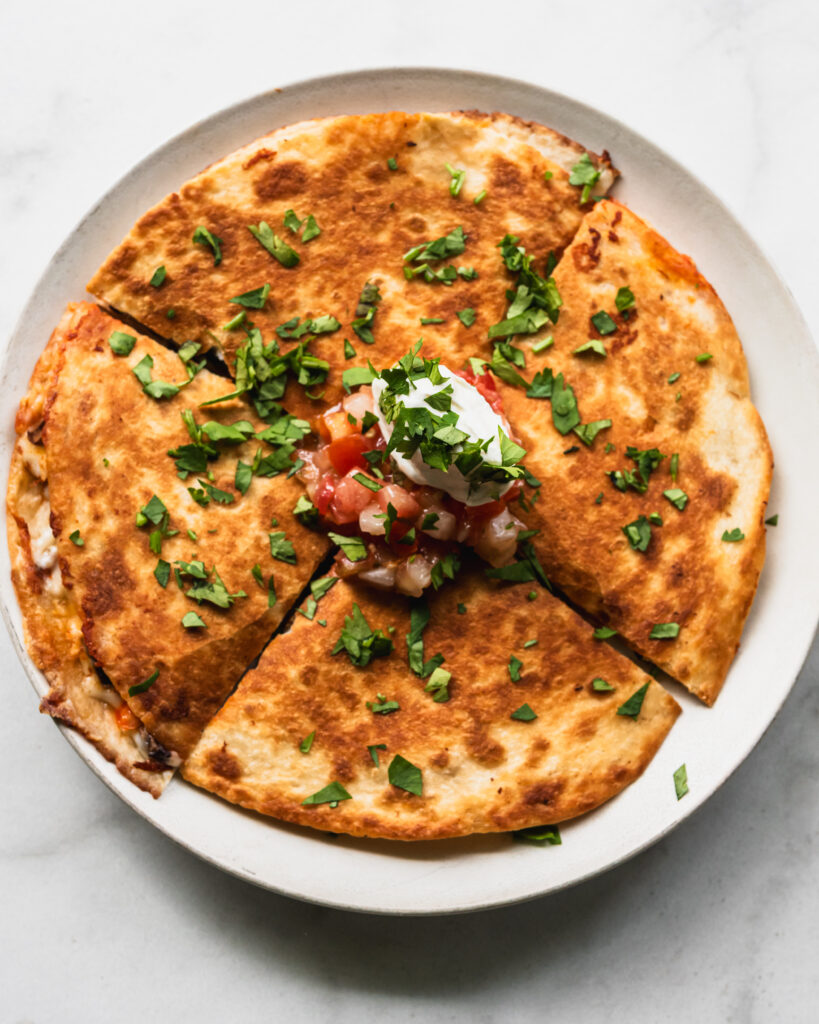 kimchi quesadilla on plate with sour cream and pico de gallo on top