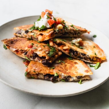 wedges of black bean kimchi quesadilla on plate with sour cream and pico de gallo