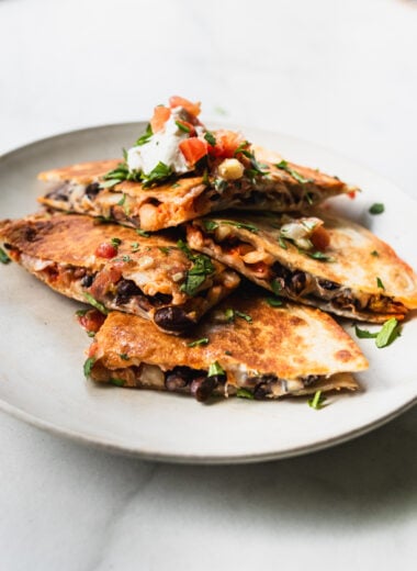 wedges of black bean kimchi quesadilla on plate with sour cream and pico de gallo