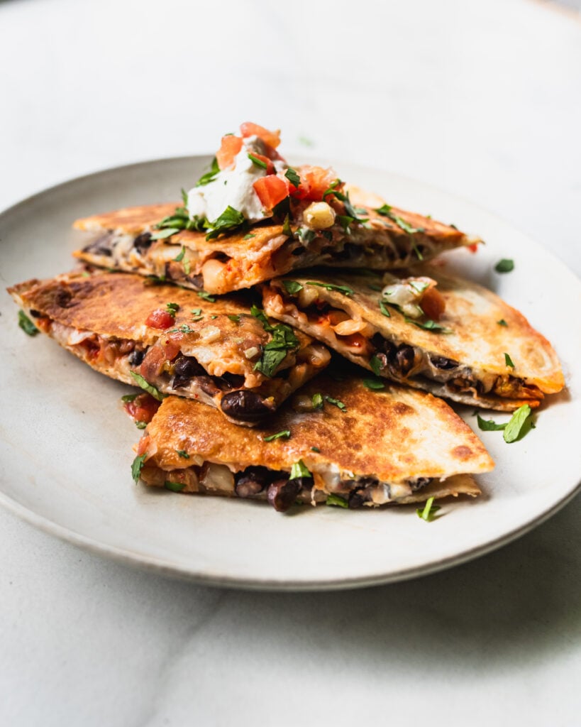 wedges of black bean kimchi quesadilla on plate with sour cream and pico de gallo