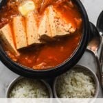 korean clay pot with kimchi jjigae and two bowls of rice and two spoons