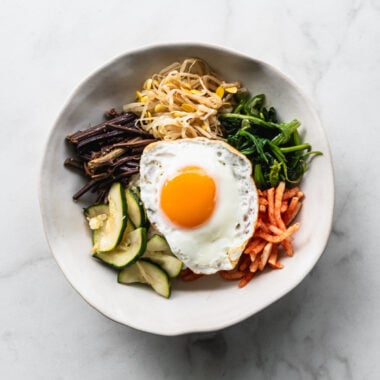 ingredients for bibimbap arranged in sections in a bowl with a fried egg on top