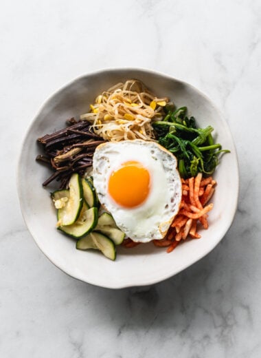 ingredients for bibimbap arranged in sections in a bowl with a fried egg on top